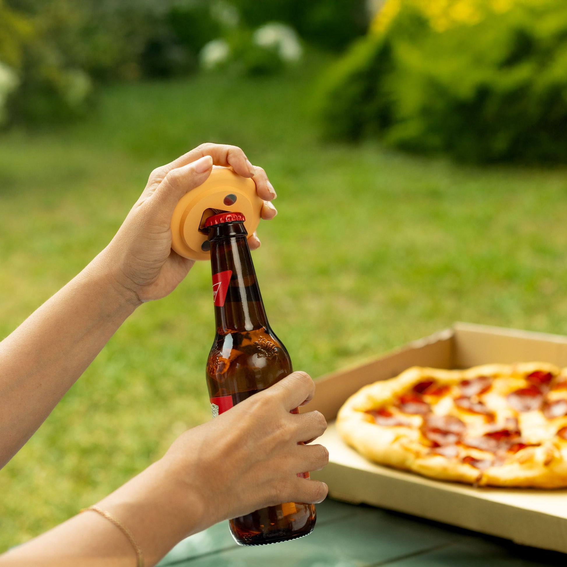 Pizza opener in outdoor picnic setting – opening beer with pizza in background